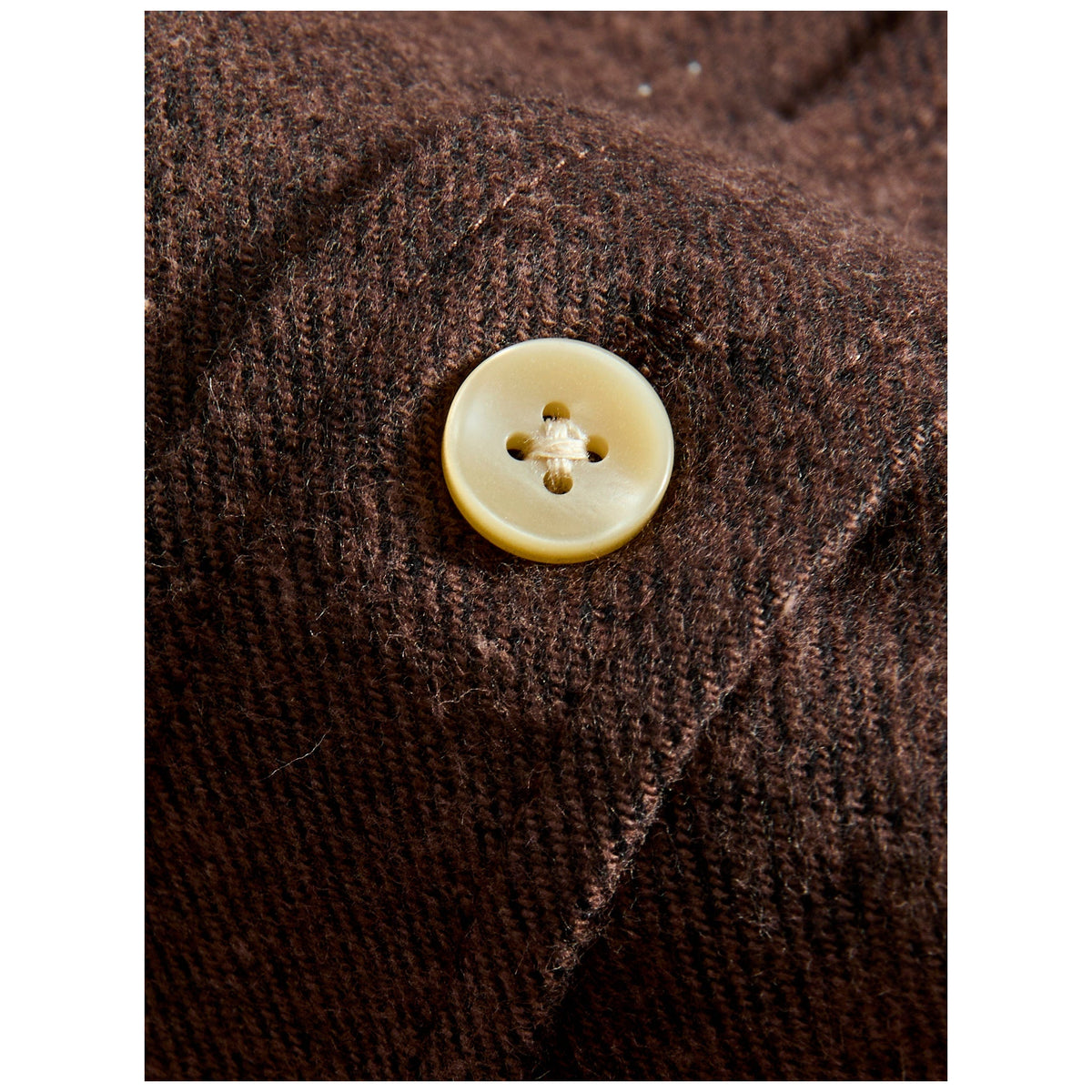 Close-up macro shot of cream mother-of-pearl button on brown flannel shirt fabric