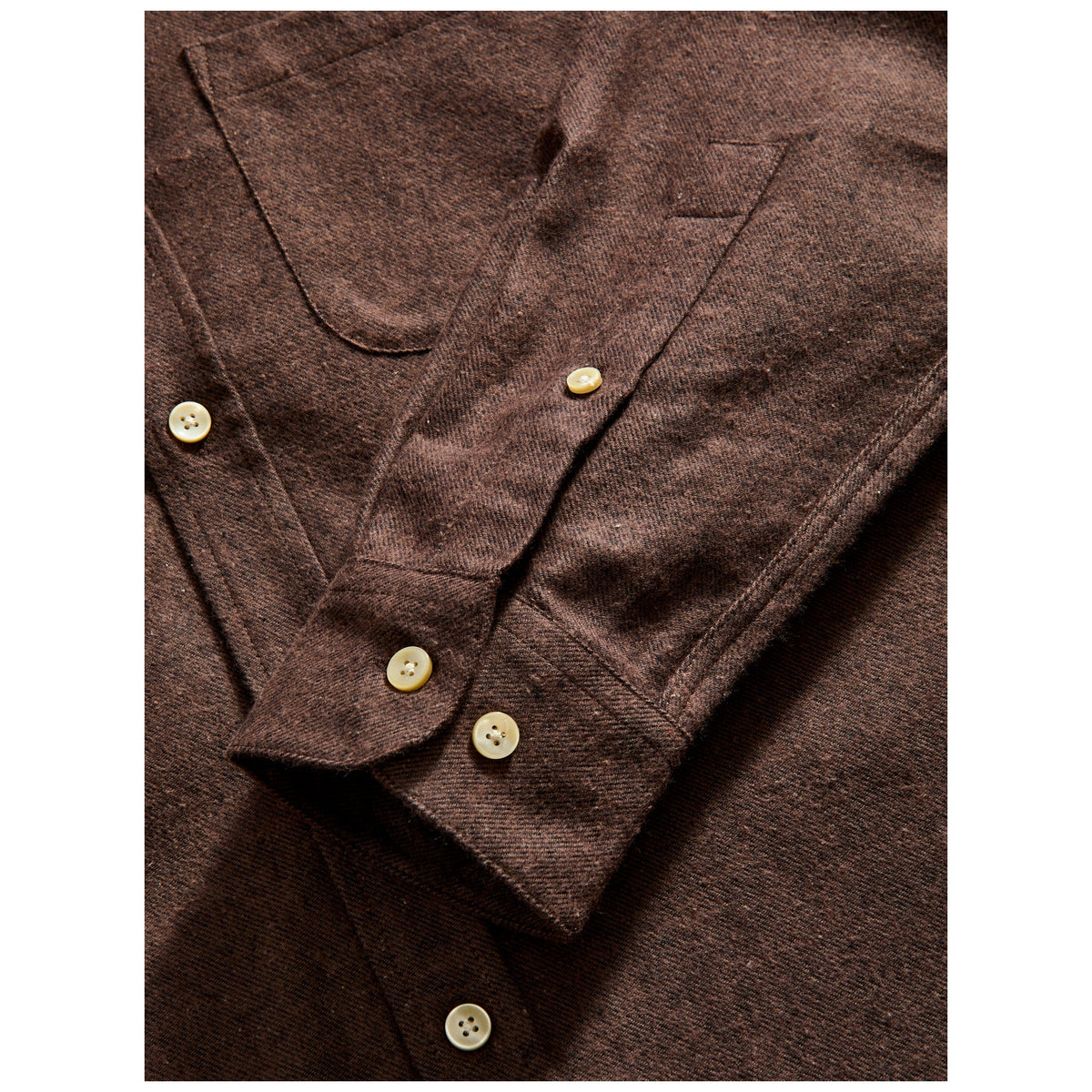 Close-up detail of brown flannel shirt showing cream buttons, chest pockets, and cuff