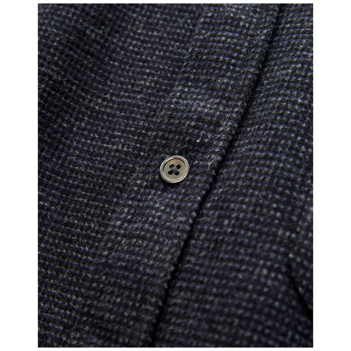 Close-up detail of dark navy blue textured wool flannel fabric with pearl button