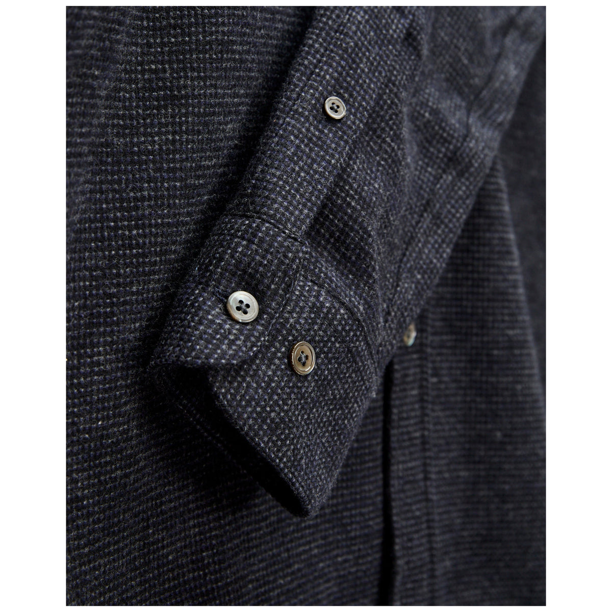 Close-up detail of dark grey textured flannel shirt sleeve with pearl buttons