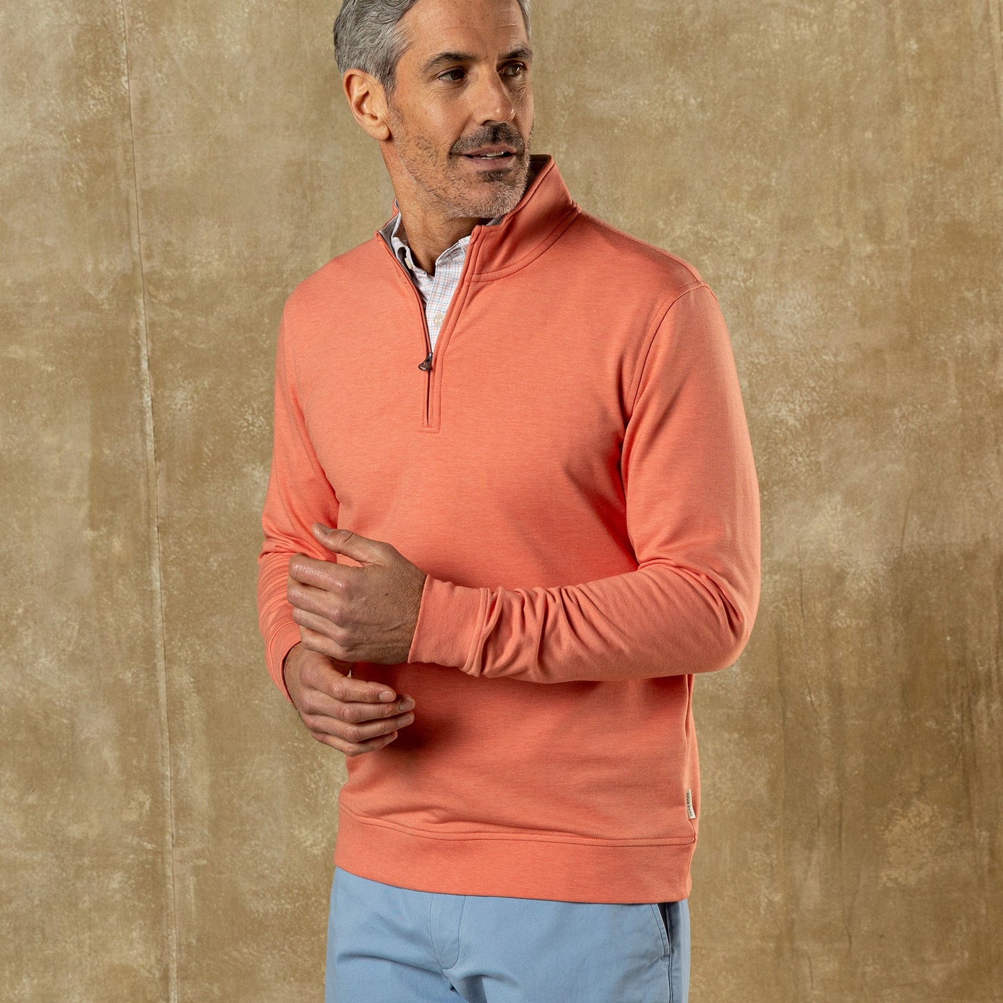 Man wearing coral heather quarter-zip pullover with blue pants against textured background