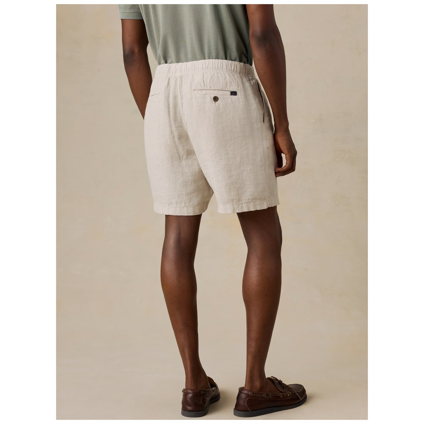 Model wearing light beige linen shorts with boat shoes from behind