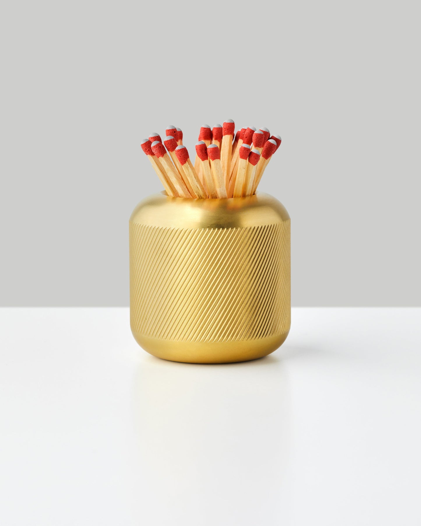 Brass cylindrical match strike holder with textured ridged surface containing red-tipped matches