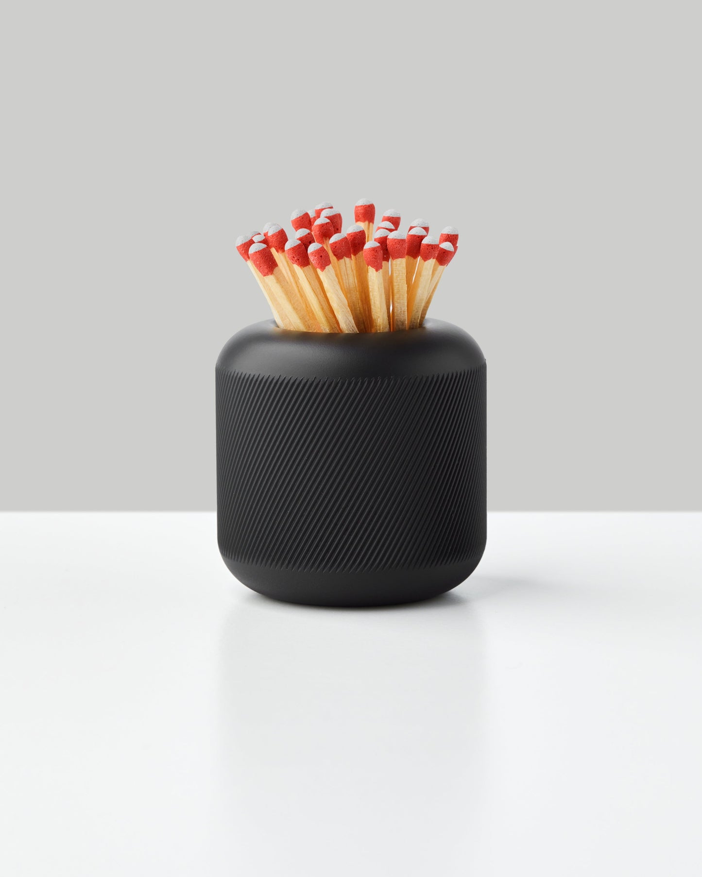 Black cylindrical match striker with textured ridged surface containing red-tipped matches