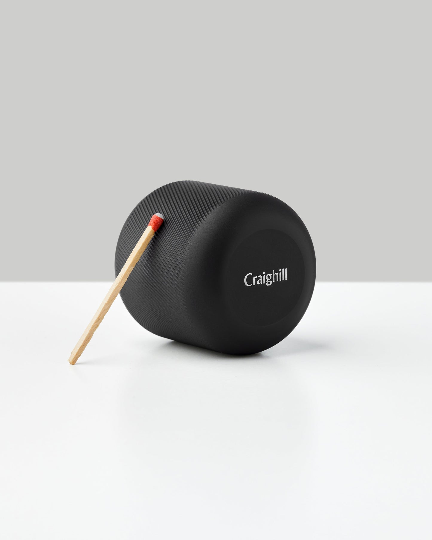 Black cylindrical match striker by Craighill with wooden matchstick on white surface