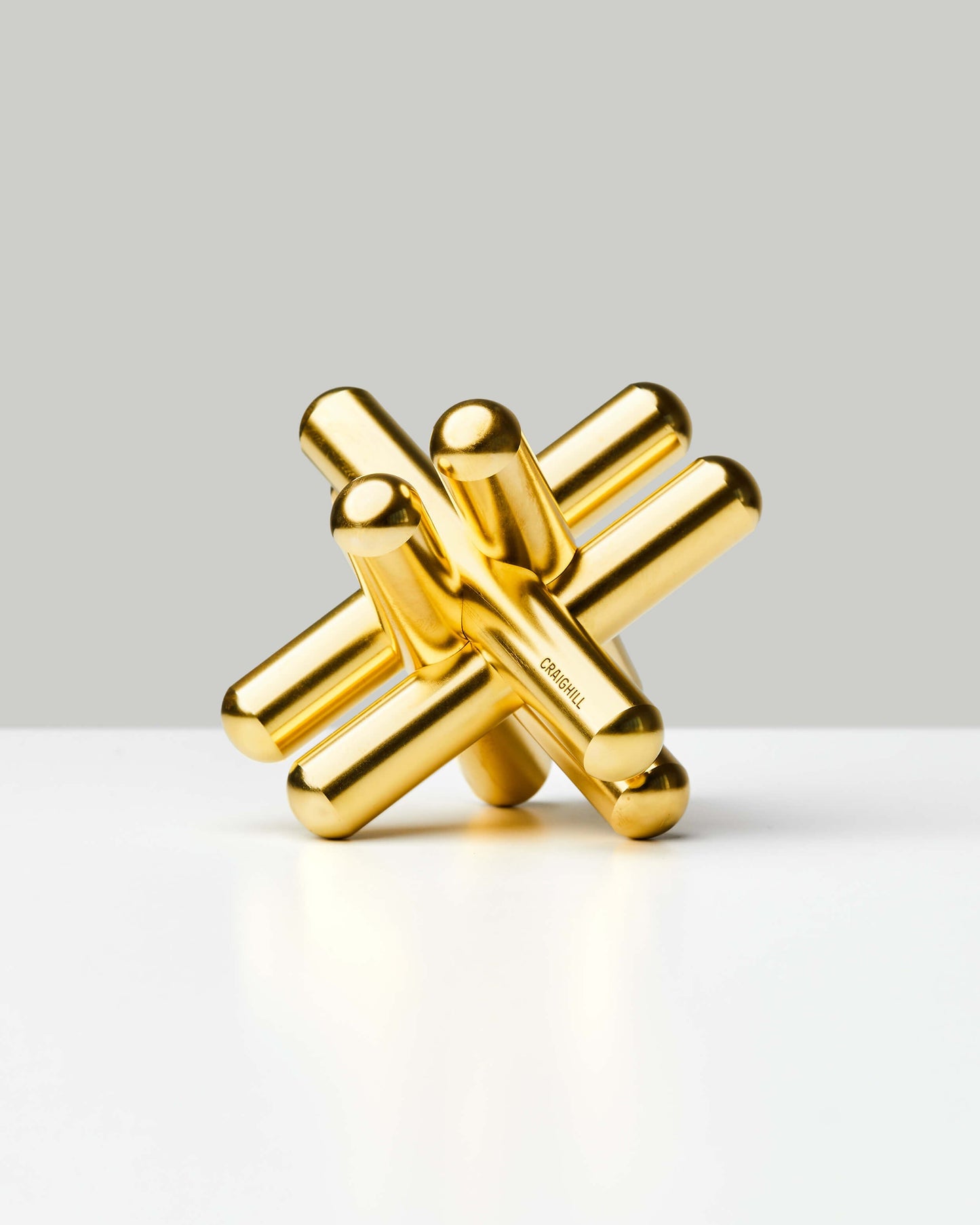 Golden brass Jack Puzzle by Craighill in three-dimensional star shape on white surface