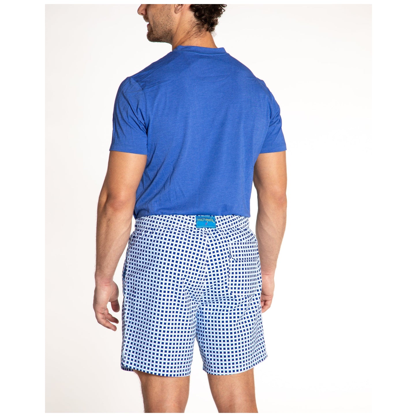 Man wearing blue t-shirt and navy white checkered swim trunks from behind