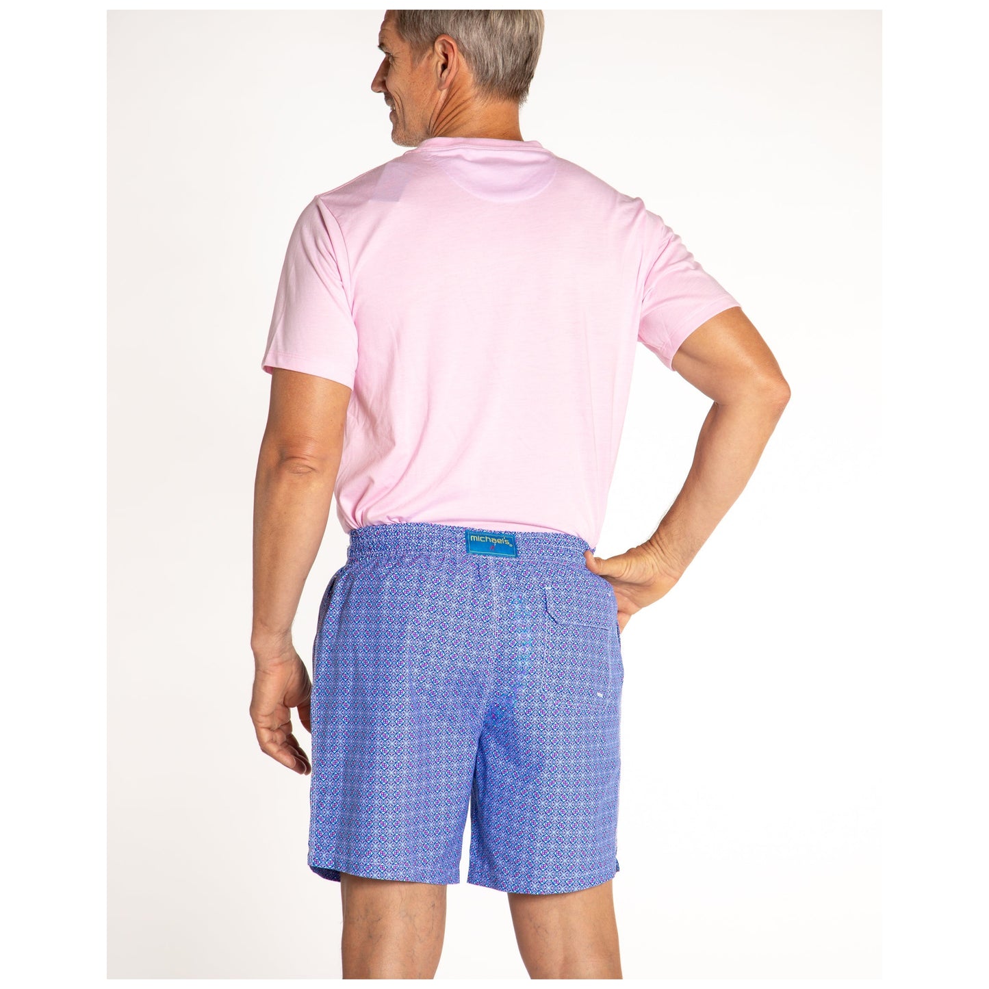 Man wearing light pink shirt and blue patterned swim trunks from behind